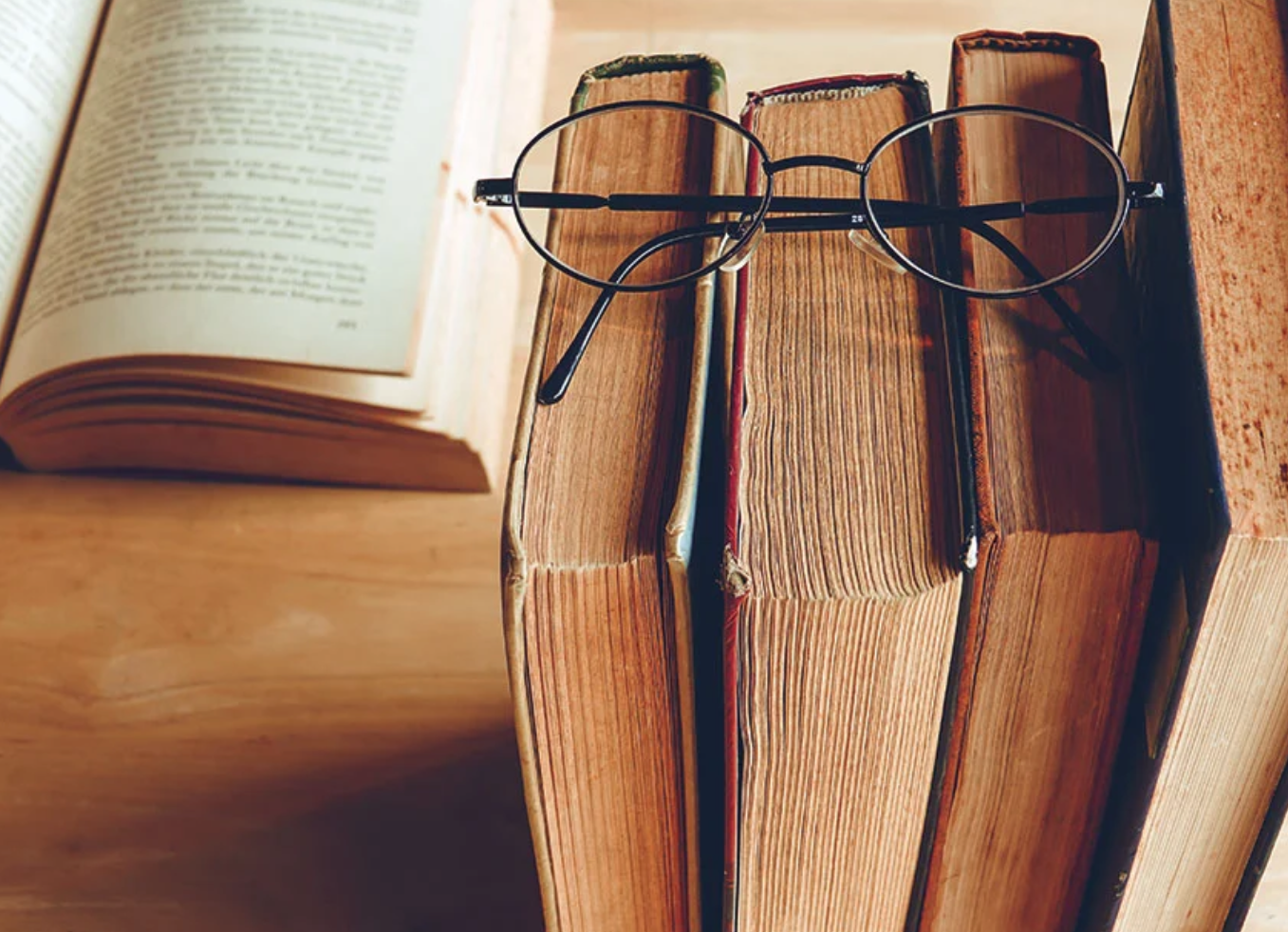 An image of the spine of several books with glasses resting on top. 